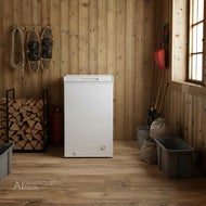 AI-genererad bild av en vit Frysbox Sunwind Nova 78l, 12/24V som står i ett förråd/uthus. På väggen hänger snöskor och ett rep, bredvid finns staplad ved. Till höger står skidstavar och en spade, och golvet är av trä.