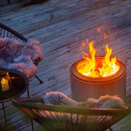 Båltunna Lava 2.0 brinnande på en altan framför två stolar.