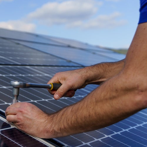 Närbild på en person som använder en hylsnyckel för att montera eller justera solpaneler under en solig dag
