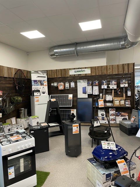 En butikshörna med Sunwind-produkter utställda, inklusive gasspisar, värmare, solpaneler och olika tillbehör, med informationsskyltar på väggen