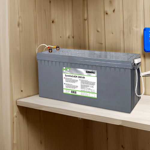Ett stort AGM-batteri från Sunwind placerat på en hylla i en träpanelad stuga. Bredvid på väggen sitter en blå Victron solcellsregulator (MPPT) med kablar kopplade till batteriet