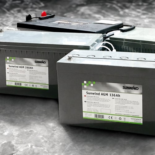Tre Sunwind-batterier av typen AGM står på ett grått betonggolv. Etiketterna visar modellbeteckningar och tekniska specifikationer