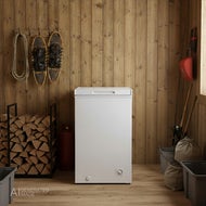 AI-genererad bild av en vit Frysbox Sunwind Nova 78l, 12/24V som står i ett förråd/uthus. På väggen hänger snöskor och ett rep, bredvid finns staplad ved. Till höger står skidstavar och en spade, och golvet är av trä.