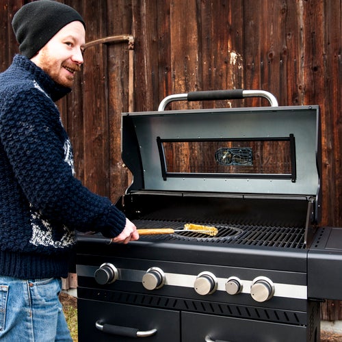 Man rengör en gasolgrill med en grillborste utomhus