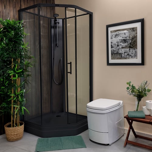 Modernt badrum med mörk duschkabin, vit El-dorado förbränningstoalett, gröna detaljer som badrumsmatta och handduk samt växter som dekoration

