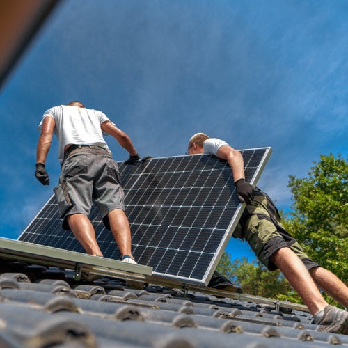 Två personer installerar solpanel på hustak under klarblå himmel